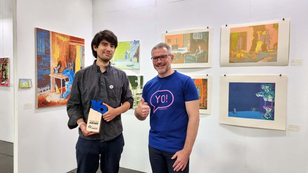 Zwei Männer stehen neben einander. Der jüngere Mann hält einen Pokal den YO-AWARD in der Hand, der andere zeigt den Daumen hoch.