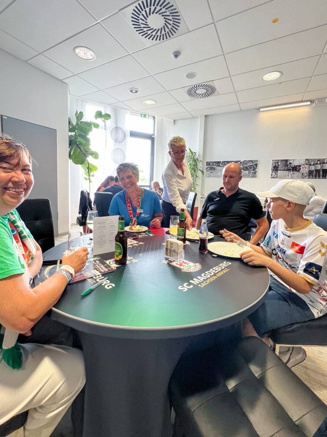 4 Personen an einem Tisch in der Klaus-Miesner-Lounge der GETEC Arena und eine Servierkraft. Zwei Personen schauen in die Kamera, zwei Personen schauen zur Hand der Servierkraft.