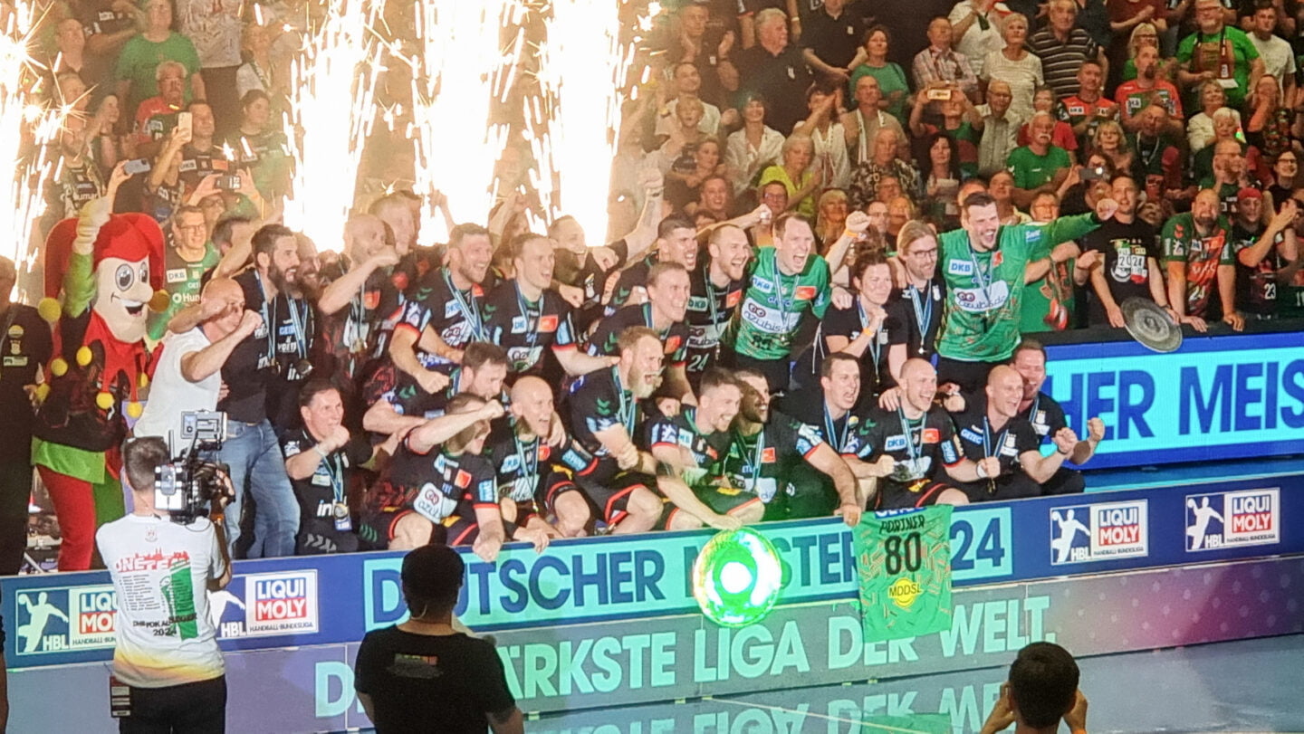 Die Mannschaft des SC Magdeburg steht in der GETEC Arena auf einer Bühne und posiert und feiert den Erhalt der Meisterschale 2024