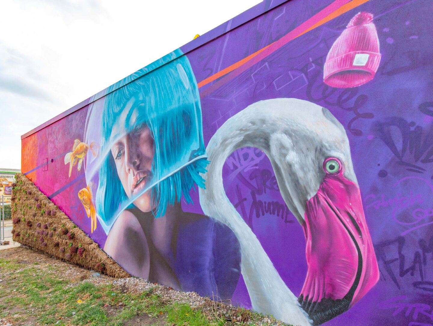 Heizhaus mit Graffitimotiv einer Frau mit blauen Haaren und einem Goldfischglas über dem Kopf. Daneben ist ein Motiv eines Flamingos.