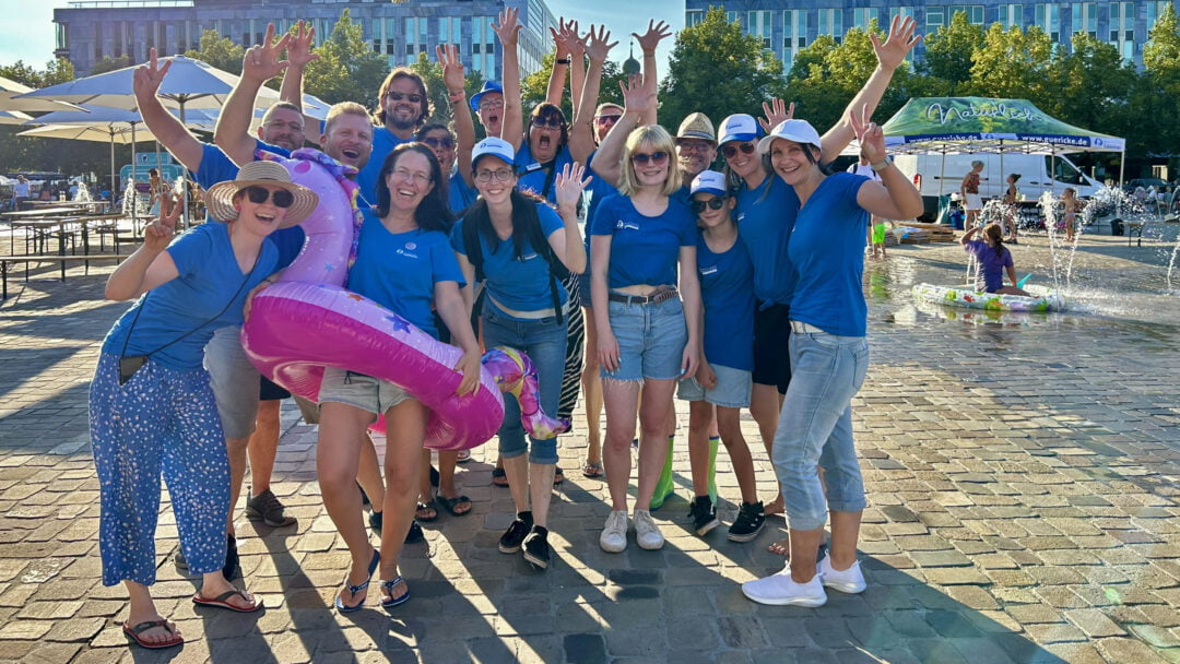 Eine größere Gruppe Menschen steht mit blauen T-Shirts auf dem Domplatz und posiert fröhlich für ein Foto.