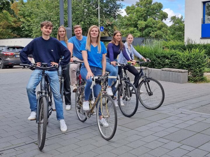 Sechs junge Menschen auf Fahrrädern, die in die Kamera lächeln.