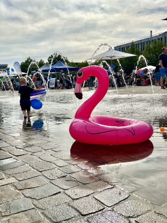 Ein Schwimmring in Form eines Flamingos auf dem Magdeburger Domplatz. Springbrunnen und ein Kind im Hintergrund