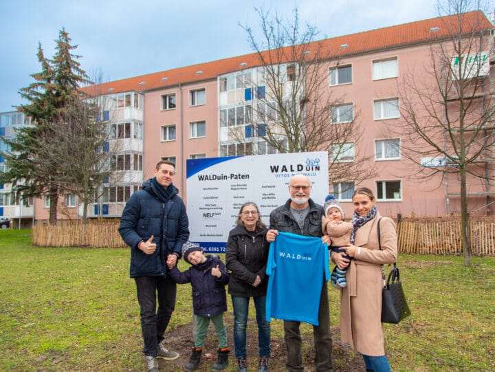 Eine Gruppe Menschen vor einem Schild mit dem Titel "WALDuin-Paten" und einem vierstöckigem Wohnhaus