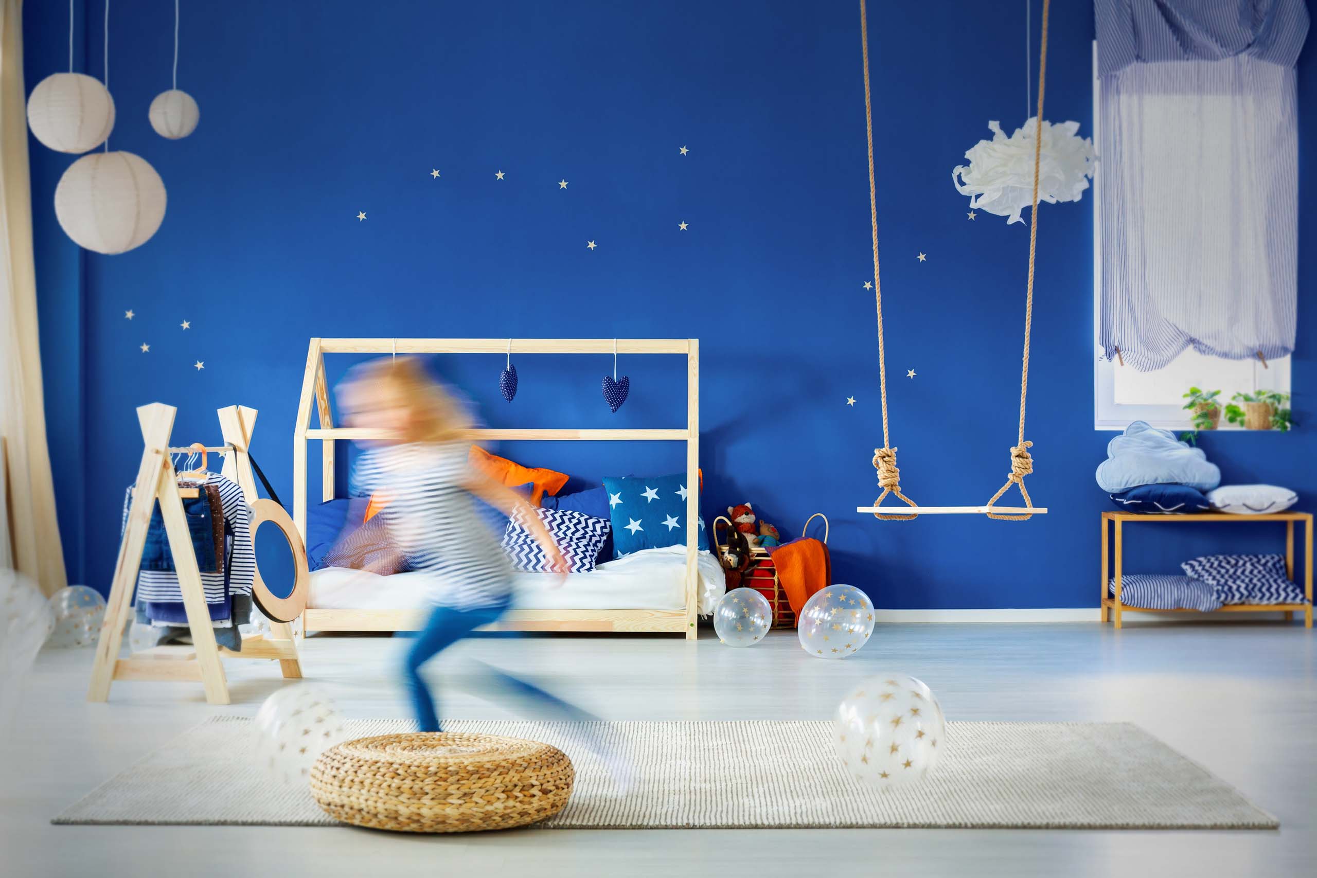 Blaues Kinderzimmer mit heller Holzeinrichtung und einem Mädchen, das spielt.