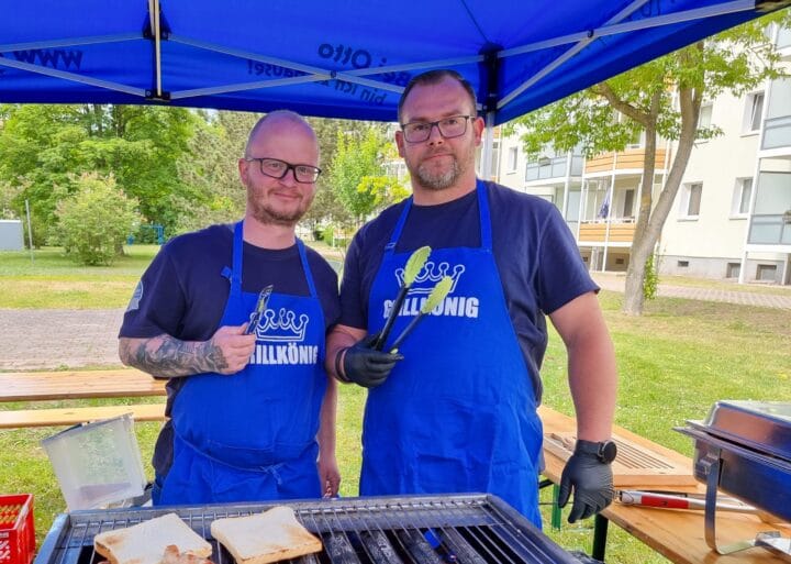 Zwei Männer mit Grillzange unter einem Pavillon